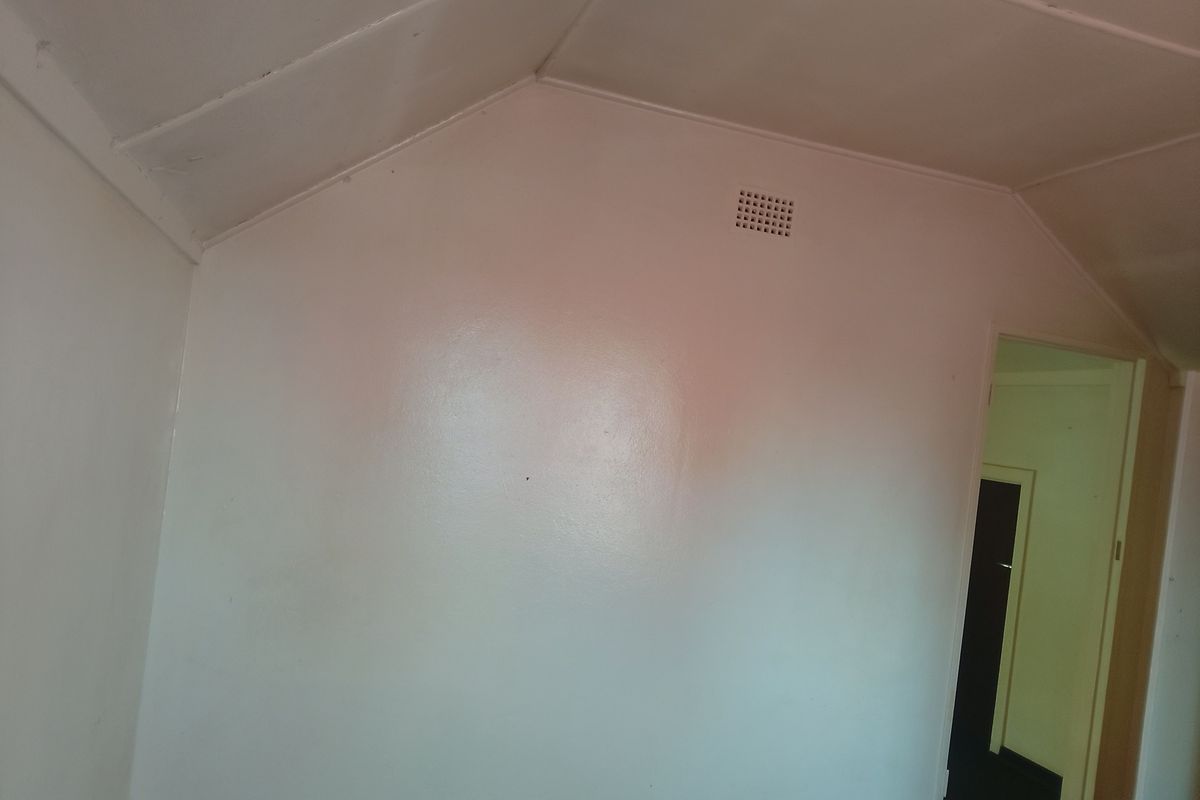 A vacant bedroom featuring a raked ceiling with visible joint lines and a wall-mounted ventilation vent.