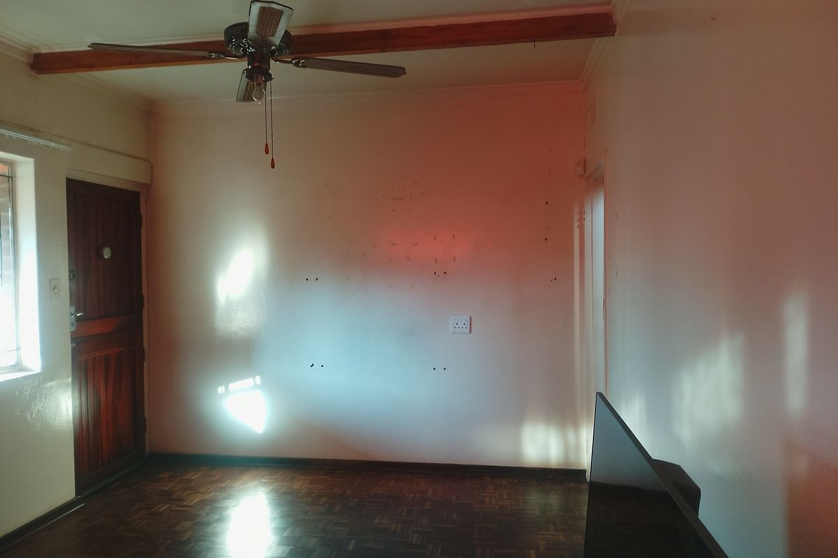 A living room featuring parquet flooring, a ceiling fan, and a wooden door, offering a blank canvas for personalization.