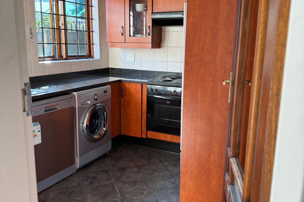 Compact kitchen featuring wooden cabinetry, dark granite countertops, tiled flooring, and integrated oven with extractor fan.