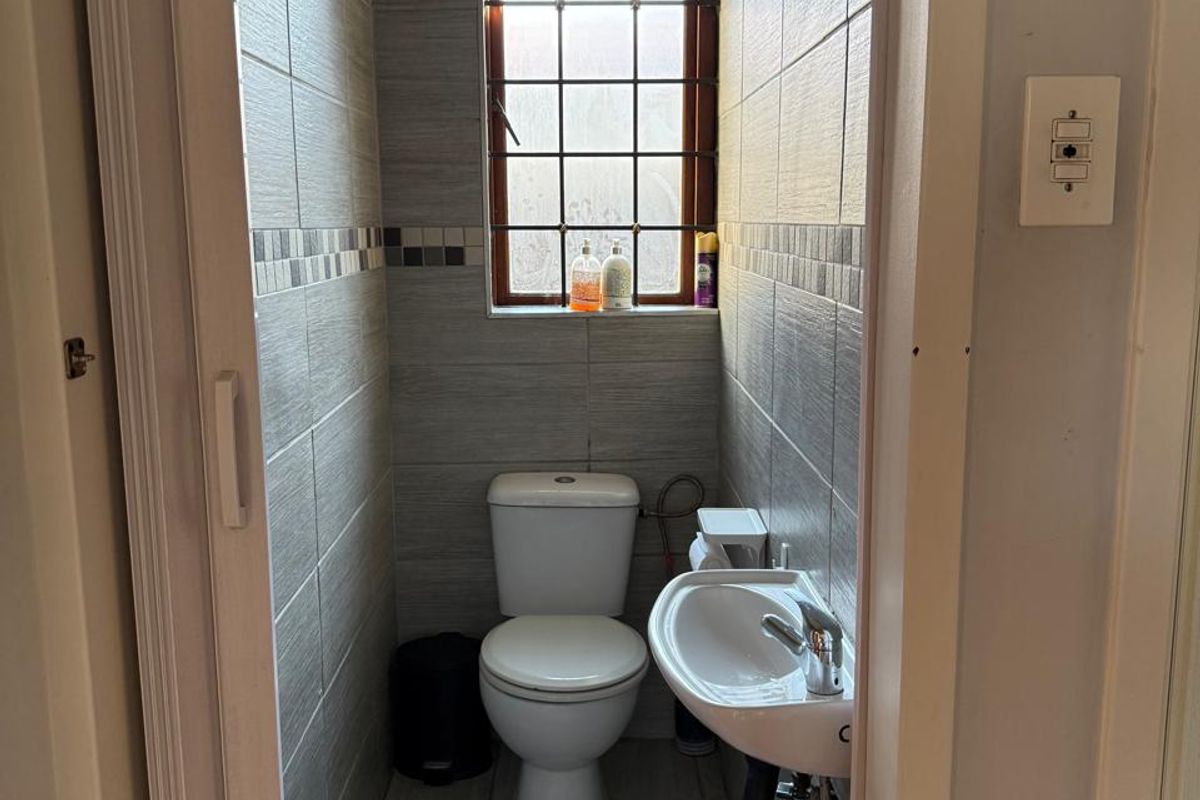 A compact guest bathroom featuring floor-to-ceiling grey tiling, a wall-mounted basin, and a standard toilet.