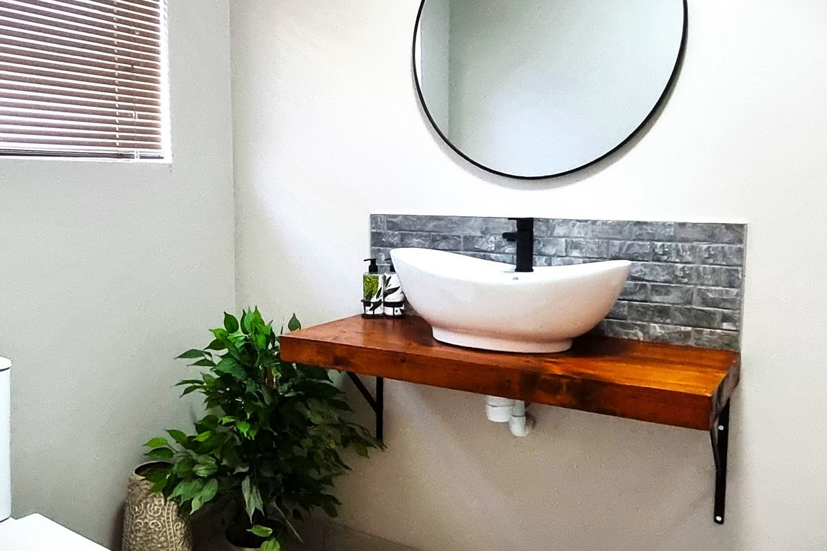 Modern bathroom featuring a floating timber vanity shelf, vessel sink, matte black tapware, and a circular wall-mounted mirror.