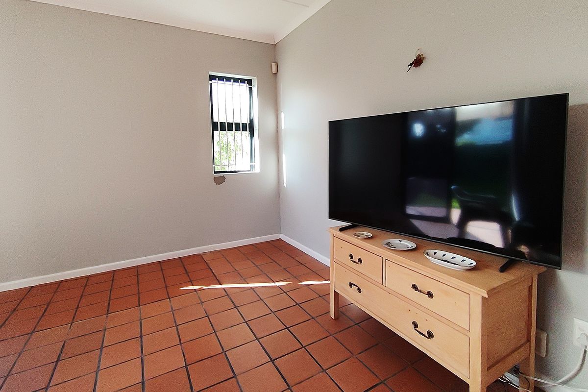 A living room featuring terracotta floor tiles and a window with security bars.