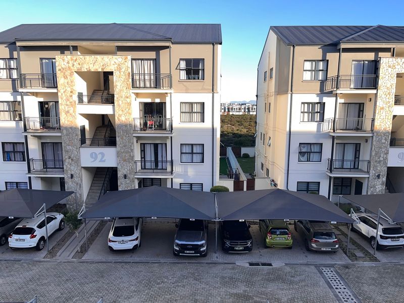 Exterior view of a modern apartment complex featuring stone-clad facades, private balconies, and covered parking bays with shade sails.