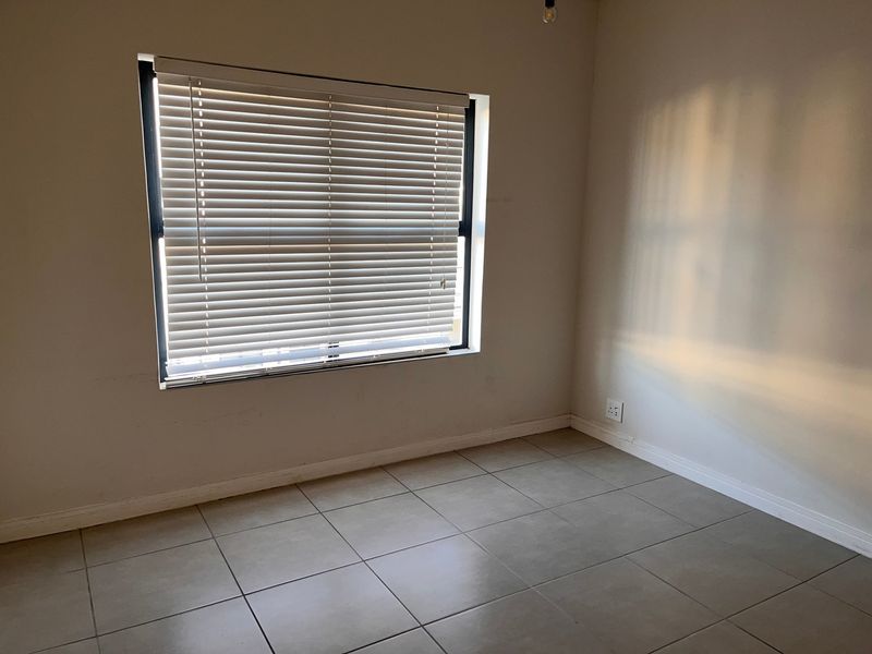 A vacant bedroom featuring neutral tiled flooring and a window fitted with venetian blinds, offering a clean and blank canvas.
