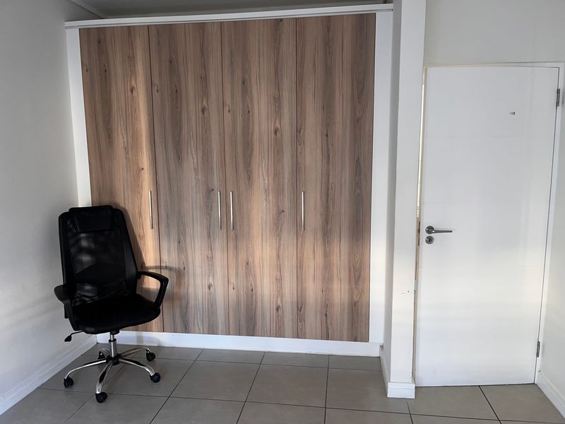 A bedroom featuring a large built-in wardrobe with wood-grain finish and neutral tiled flooring.