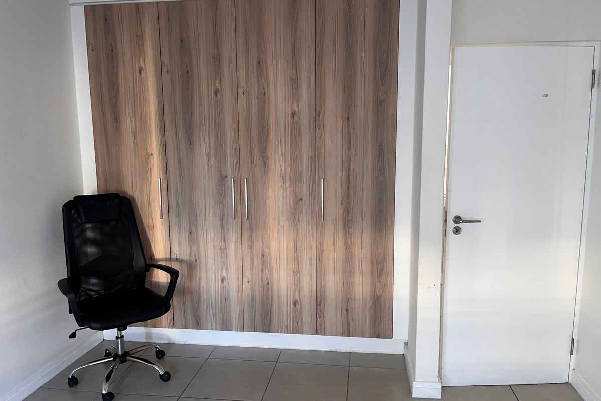 A bedroom featuring a large built-in wardrobe with wood-grain finish and neutral tiled flooring.