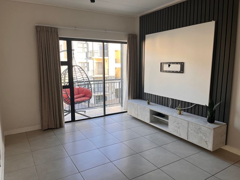 A bright living room featuring large format floor tiles, a modern slatted feature wall, and a built-in media console with access to a balcony.
