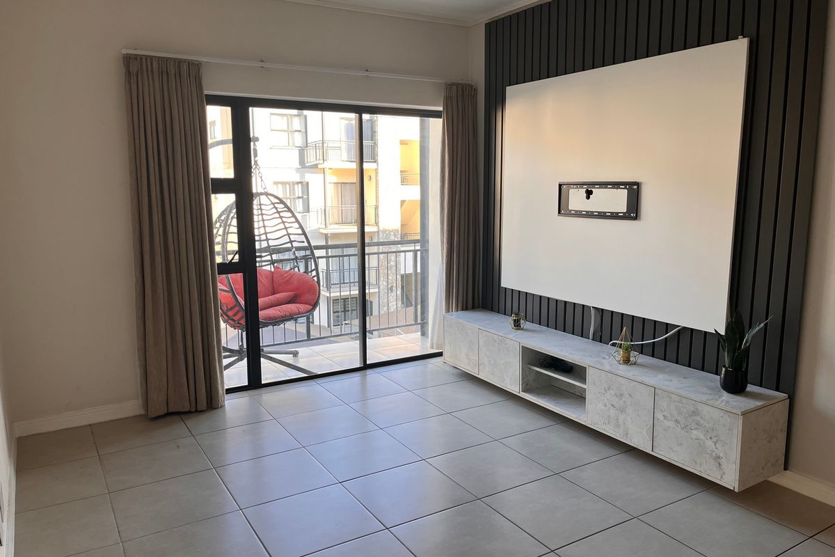 A bright living room featuring large format floor tiles, a modern slatted feature wall, and a built-in media console with access to a balcony.