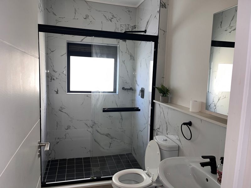 Modern bathroom featuring a walk-in shower with black-framed glass enclosure, marble-look wall tiles, and contemporary black fixtures.
