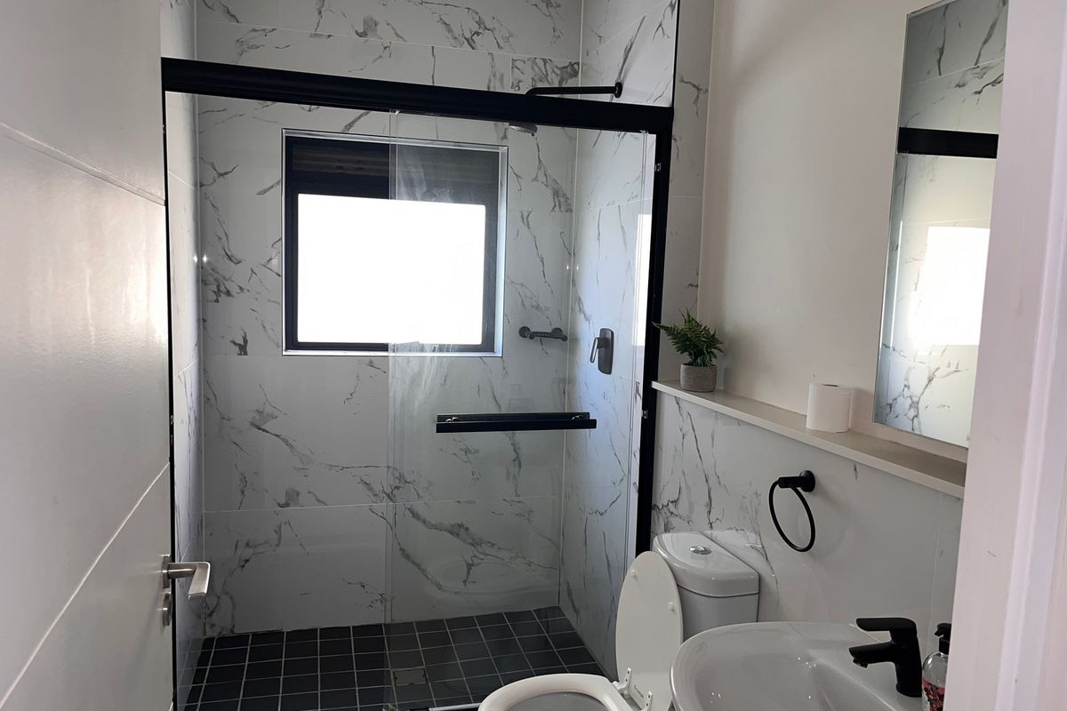 Modern bathroom featuring a walk-in shower with black-framed glass enclosure, marble-look wall tiles, and contemporary black fixtures.