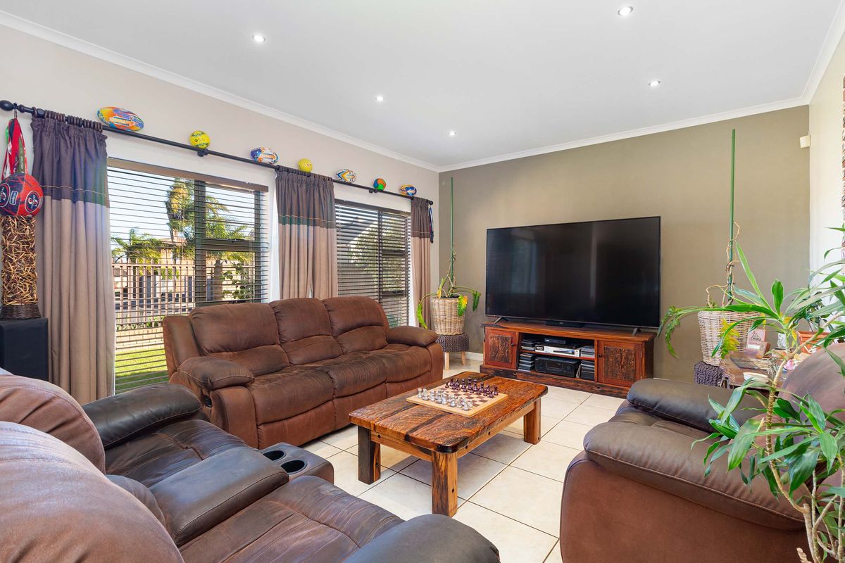 A comfortable living room featuring large windows with blinds, tiled flooring, and recessed downlighting, creating a bright and inviting space for relaxation.