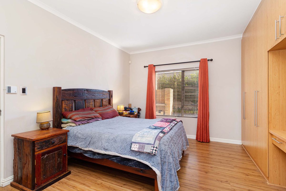 A well-maintained bedroom featuring laminate wood flooring, built-in wooden cabinetry with integrated desk space, and a window with fitted blinds.