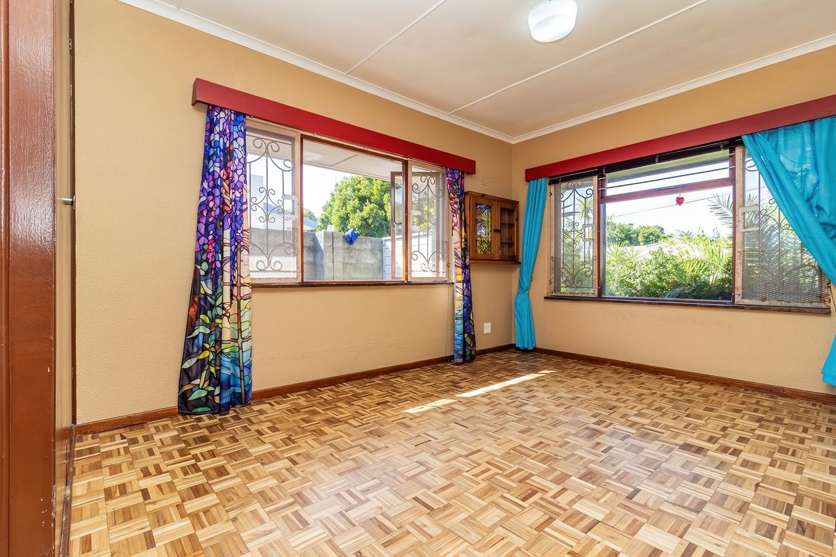 A bright, empty bedroom featuring parquet flooring, large windows with security bars, and built-in wall cabinetry.
