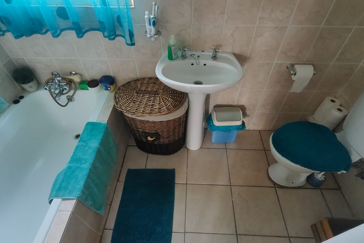 A functional bathroom featuring a standard bathtub, pedestal basin, and toilet with neutral wall and floor tiling.
