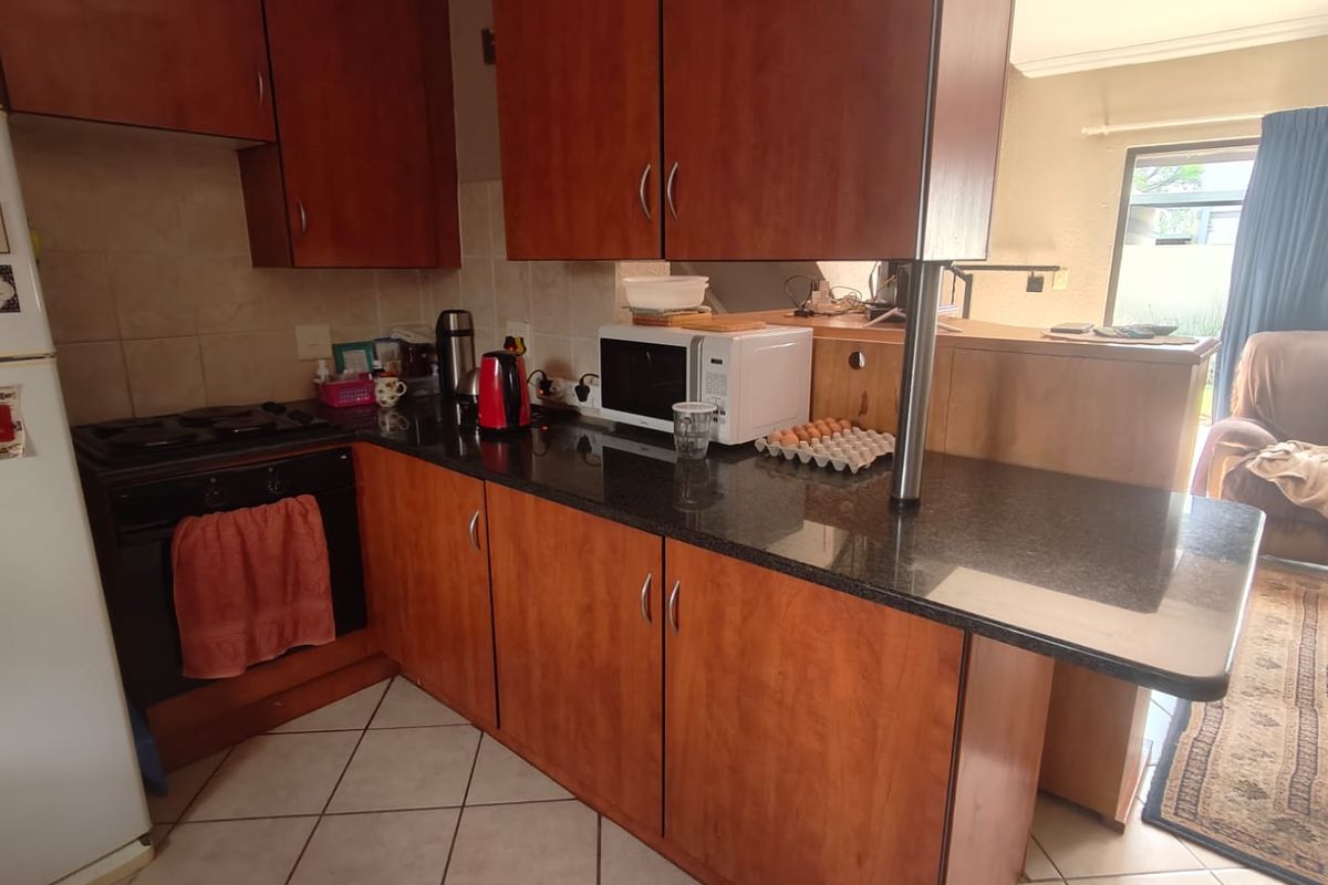 A functional kitchen featuring dark granite countertops, wooden cabinetry, and a built-in oven with a gas hob, opening into the adjacent living area.