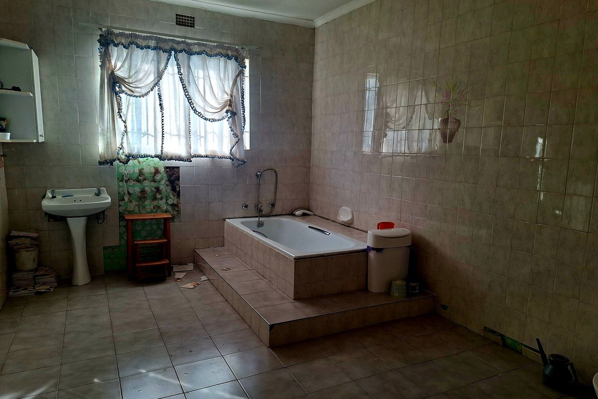 A dated bathroom featuring a built-in tiled bathtub, pedestal basin, and full-height wall tiling, requiring renovation to modernize the space.