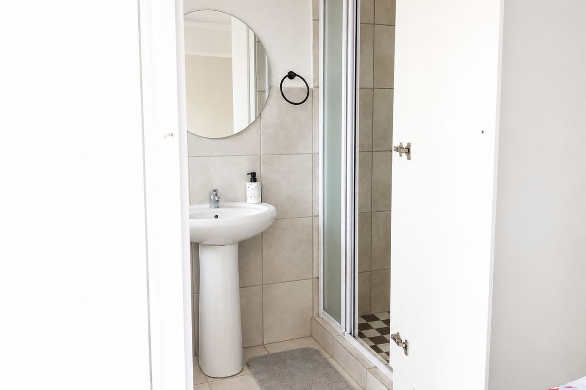 A compact bathroom featuring a pedestal basin, circular wall mirror, and a shower enclosure with tiled walls and flooring.