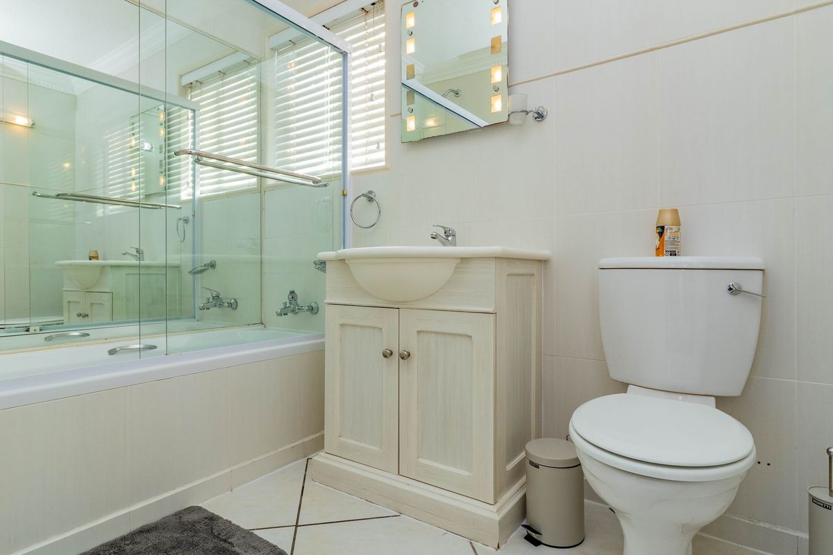 A functional bathroom featuring a built-in vanity, a bathtub with a glass shower screen, and a standard toilet with neutral wall and floor tiling.