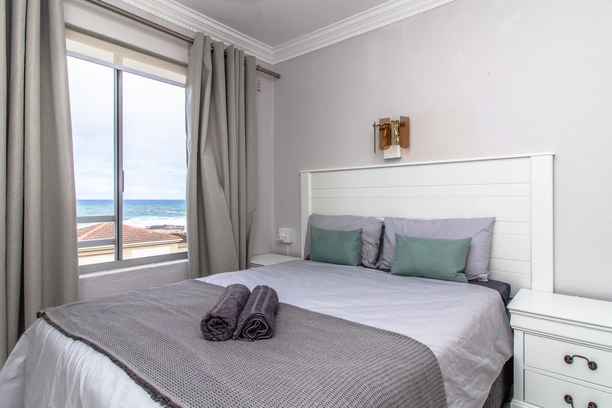 A well-maintained bedroom featuring crown molding, a wall-mounted light fixture, and a sliding window with a scenic ocean view.