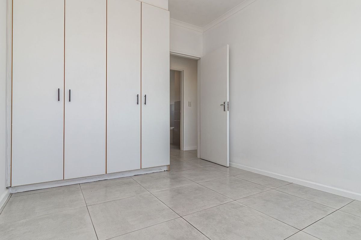 A bright, empty bedroom featuring neutral floor tiles and built-in white wardrobes, offering a clean and versatile space.