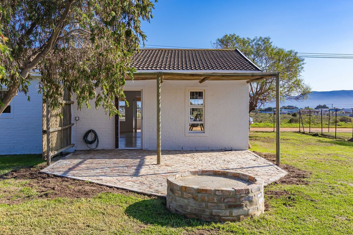 A rear view of the property featuring a paved patio area with a built-in brick fire pit and a covered pergola structure.
