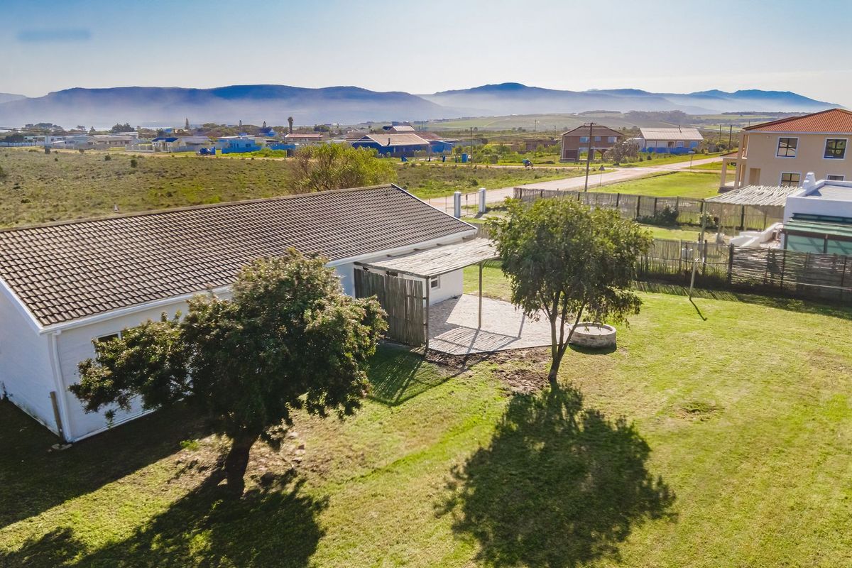 Aerial view of a residential property featuring a tiled roof, a covered patio area, and a spacious lawn with mature trees.