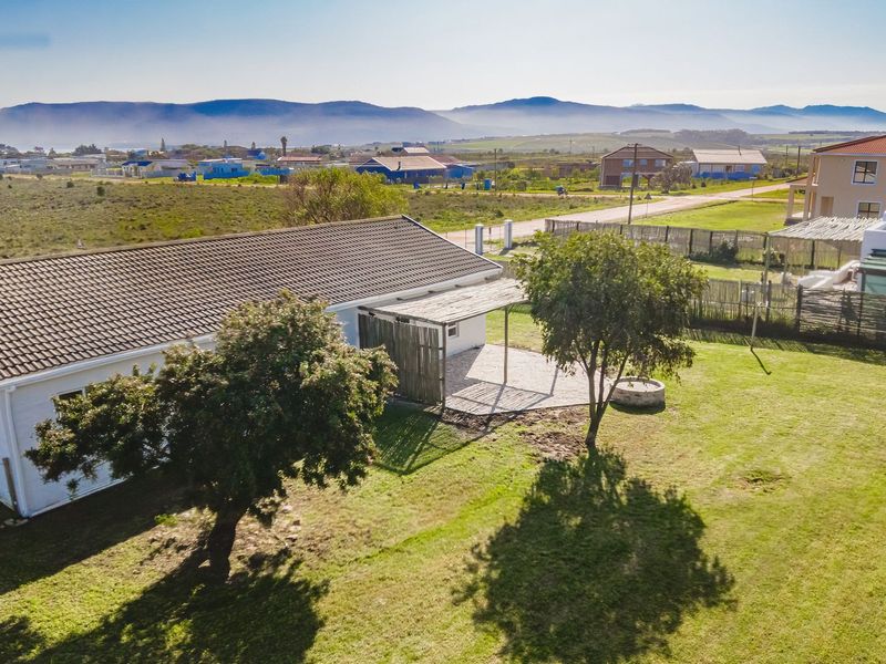 Aerial view of a residential property featuring a tiled roof, a covered patio area, and a spacious lawn with mature trees.