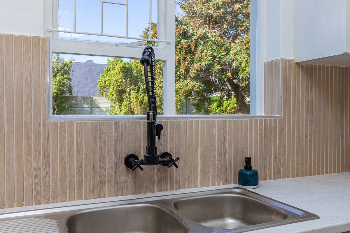 A kitchen sink area featuring a modern black gooseneck faucet, stainless steel double basin, and vertical textured tile backsplash under a window.