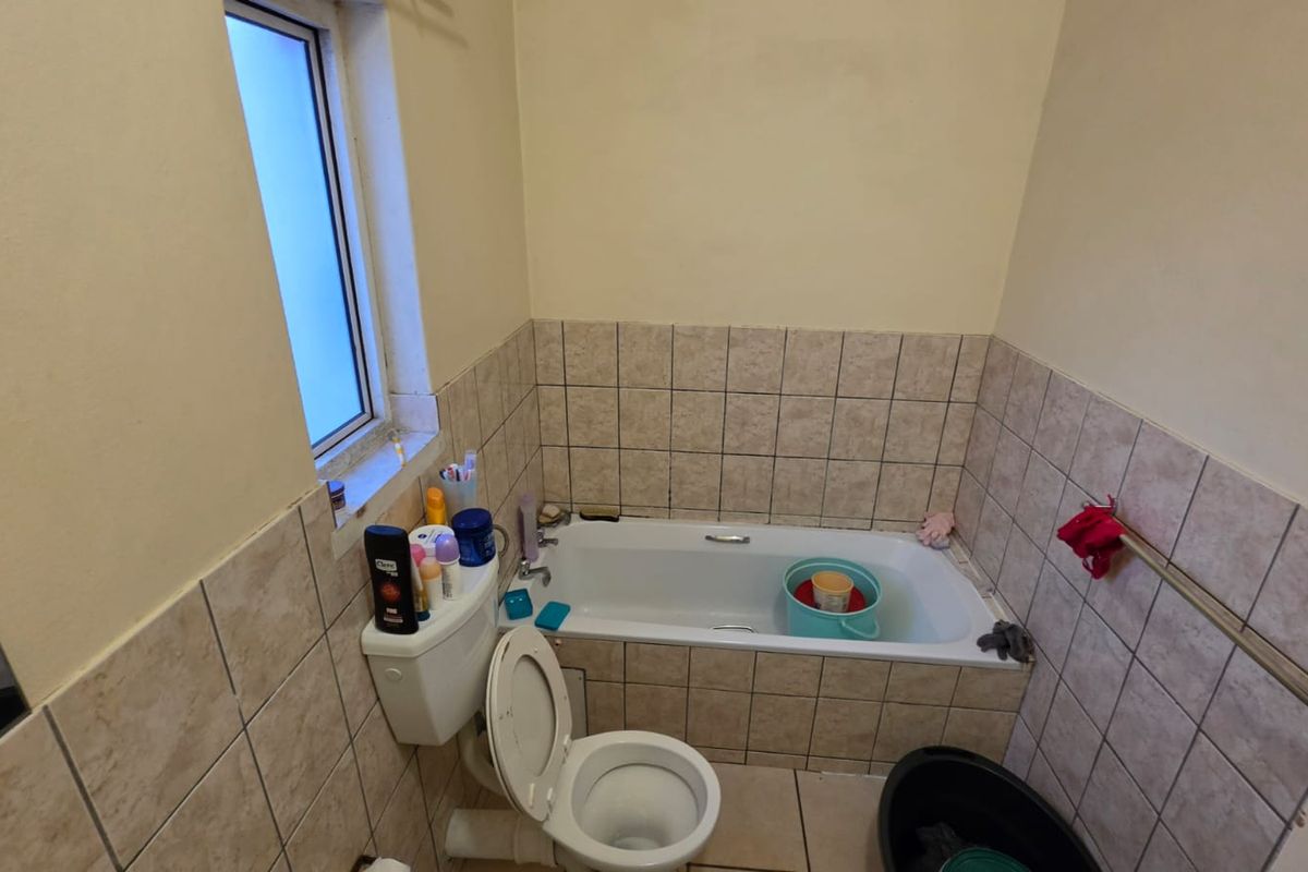 A compact bathroom featuring a standard bathtub, toilet, and tiled splashbacks. The space is functional but would benefit from cosmetic updates.