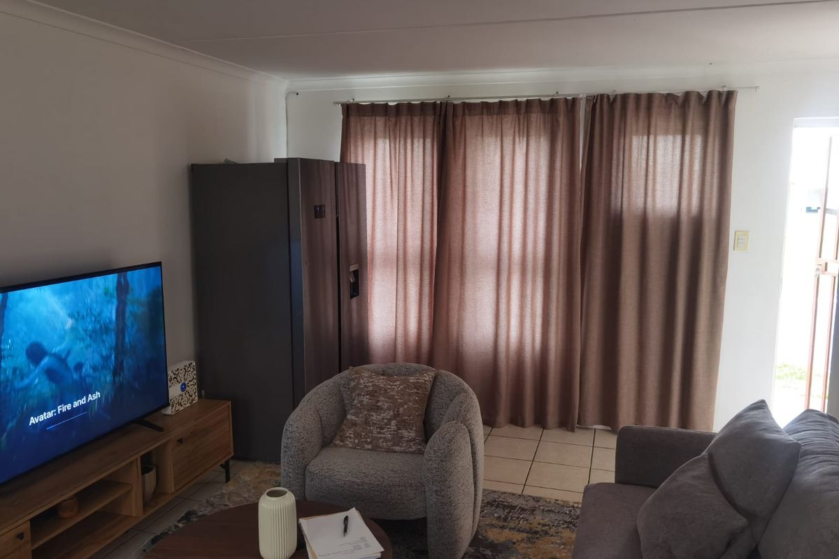 A living room area featuring tiled flooring, neutral wall finishes, and large window treatments, providing a functional and comfortable space.