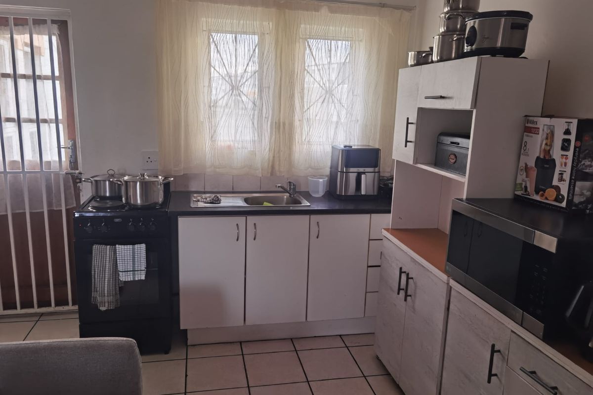 Functional kitchen featuring white cabinetry, a stainless steel sink, tiled flooring, and a freestanding stove, with direct access to an exterior door.