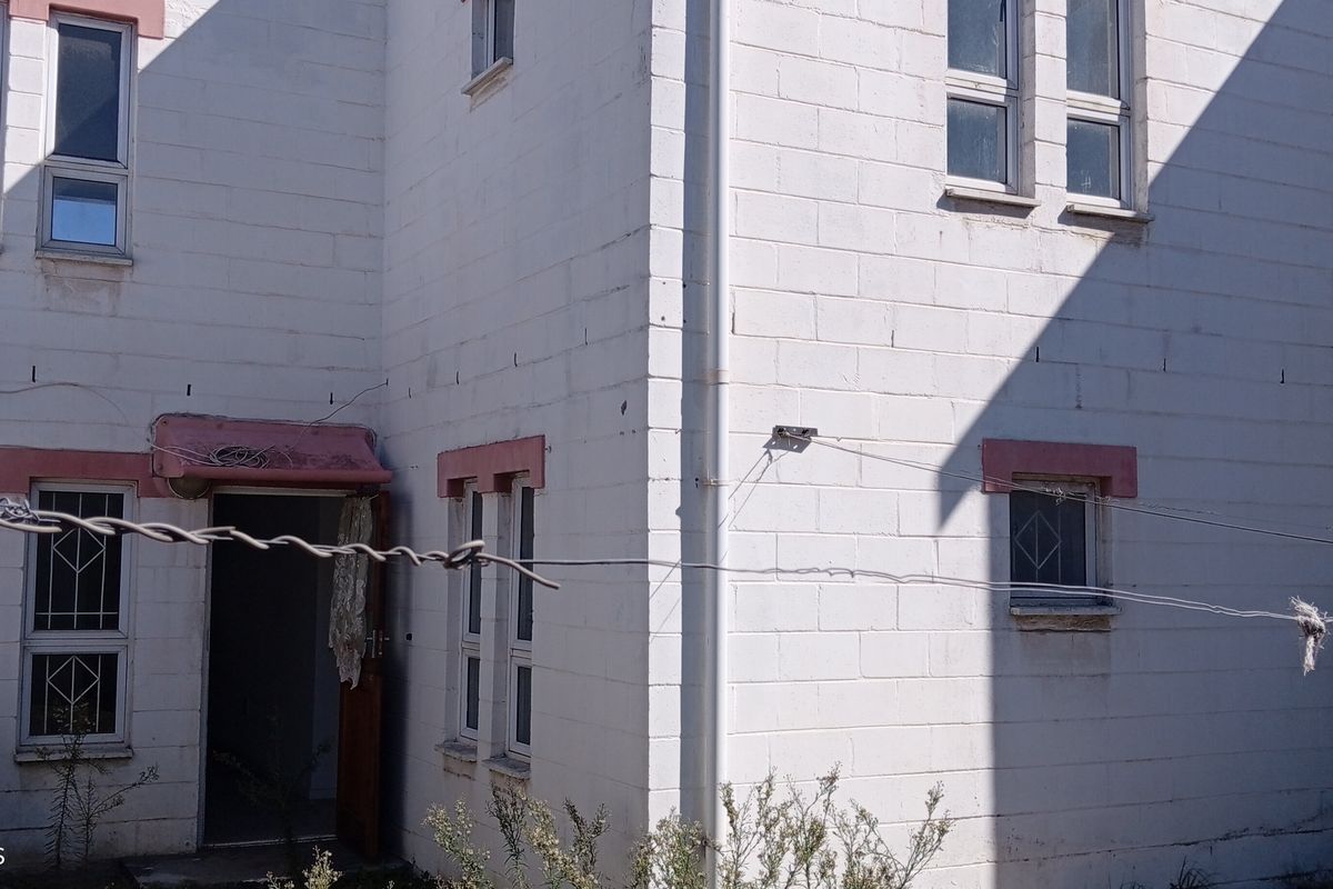 Rear exterior view of a two-story concrete block house featuring aluminium windows with security bars and a satellite dish installation.