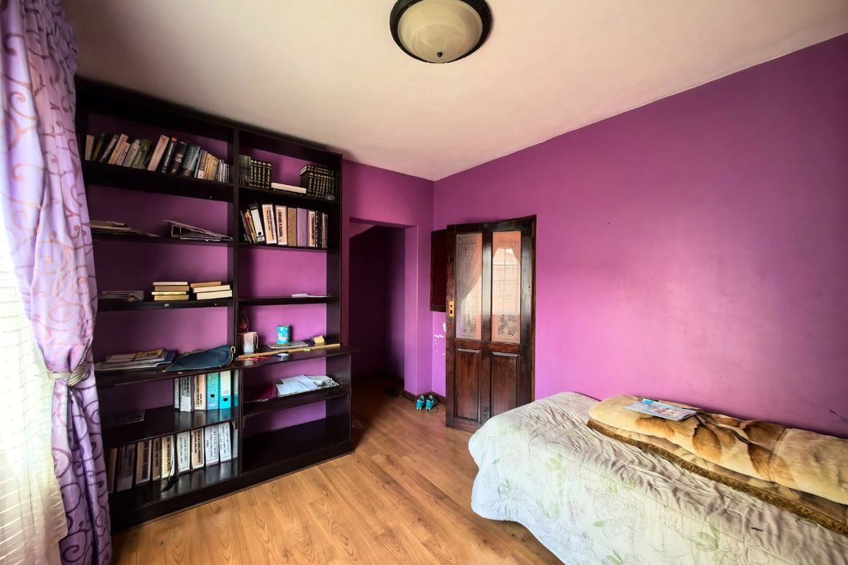 A bedroom featuring laminate flooring, a built-in dark wood bookshelf, and a wooden door with glass inserts.