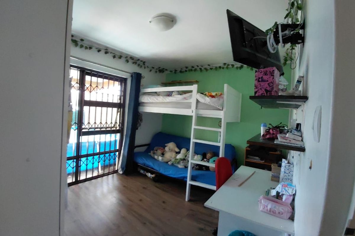 A bedroom featuring laminate flooring, a green accent wall, and a security gate on the window.