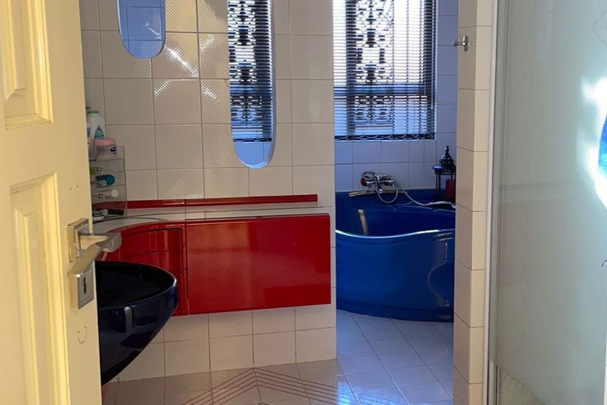 A dated bathroom featuring a blue corner bathtub, a red vanity unit, and patterned floor tiles with a shower enclosure.