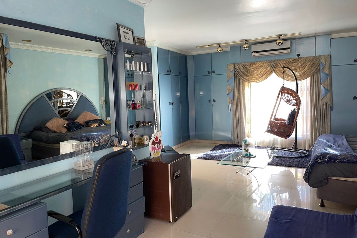 Spacious bedroom featuring extensive built-in blue cabinetry, integrated vanity unit, and wall-mounted air conditioning unit with polished tile flooring.