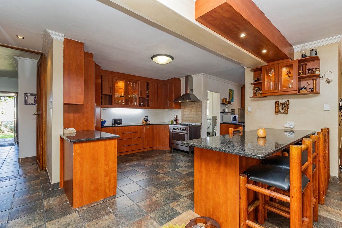 A functional kitchen featuring warm wooden cabinetry, granite countertops, a breakfast bar, and a stainless steel extractor fan with tiled flooring throughout.