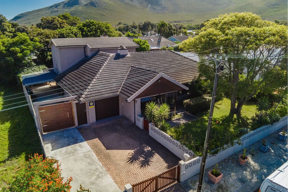 Aerial view of a residential property featuring a tiled roof, paved driveway, garage, and established garden with mountain backdrop.