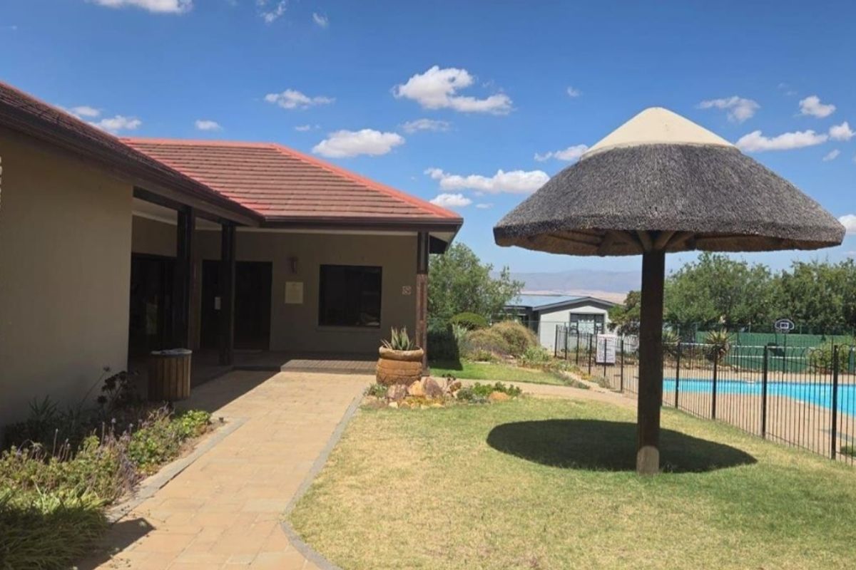 Exterior view of the property featuring a paved walkway, landscaped garden area, and a thatched umbrella structure adjacent to a fenced swimming pool.