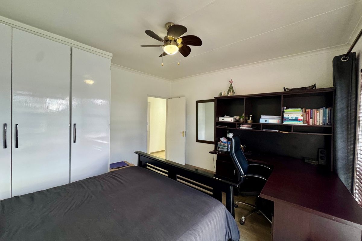 A functional bedroom featuring built-in white wardrobes, a ceiling fan, and neutral finishes, providing a comfortable and practical living space.