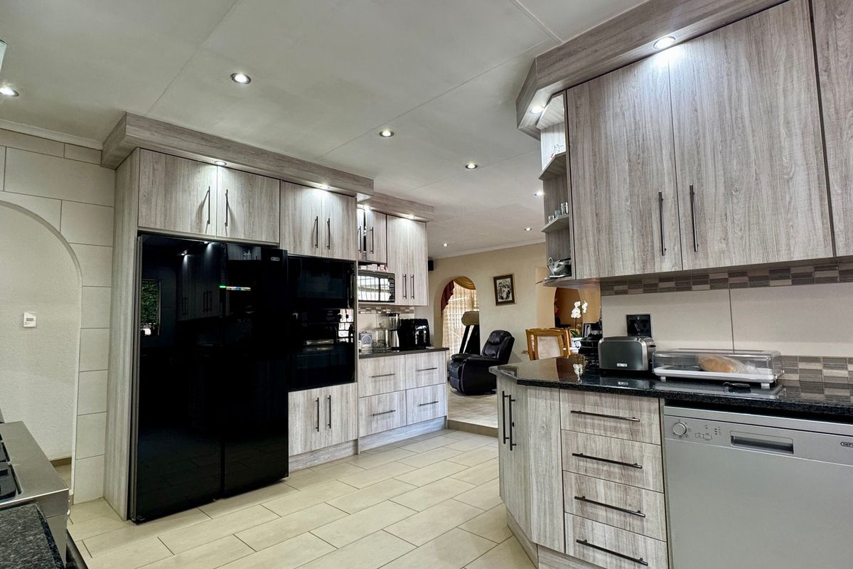 Modern kitchen featuring light wood-grain cabinetry, granite countertops, integrated appliances, and recessed ceiling lighting, flowing into an adjacent living area.