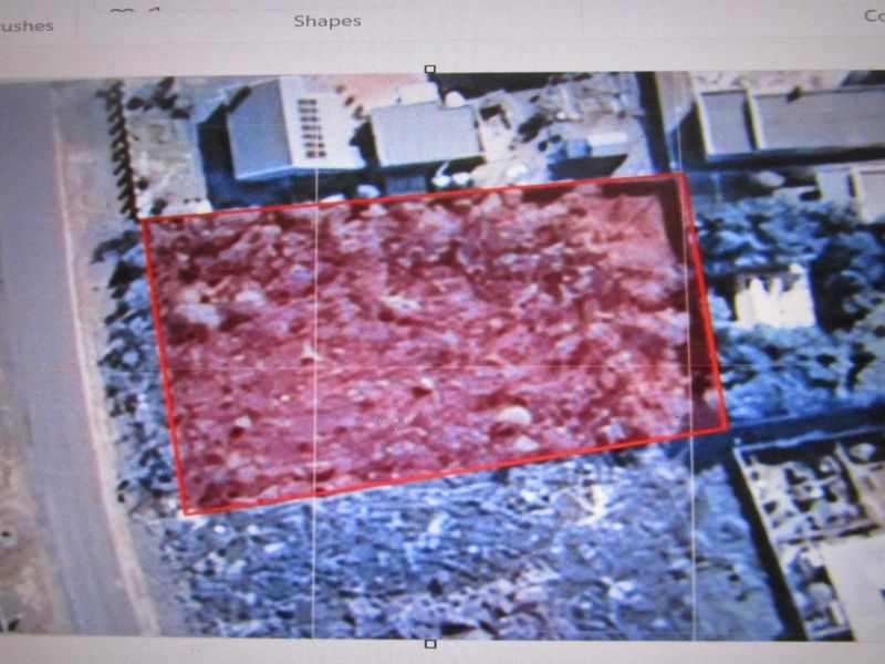 An aerial view of a vacant residential plot highlighted with a red boundary, showing surrounding neighborhood context and existing vegetation.