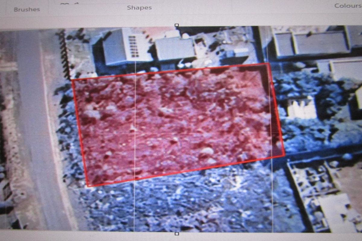 An aerial view of a vacant residential plot highlighted with a red boundary, showing surrounding neighborhood context and existing vegetation.