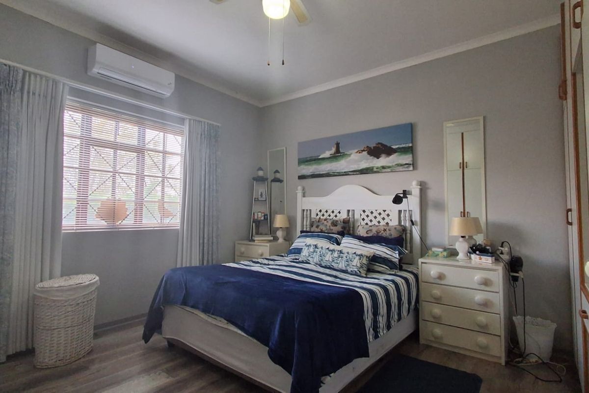 A well-maintained bedroom featuring laminate flooring, a ceiling fan, a split-system air conditioner, and built-in wardrobe storage.