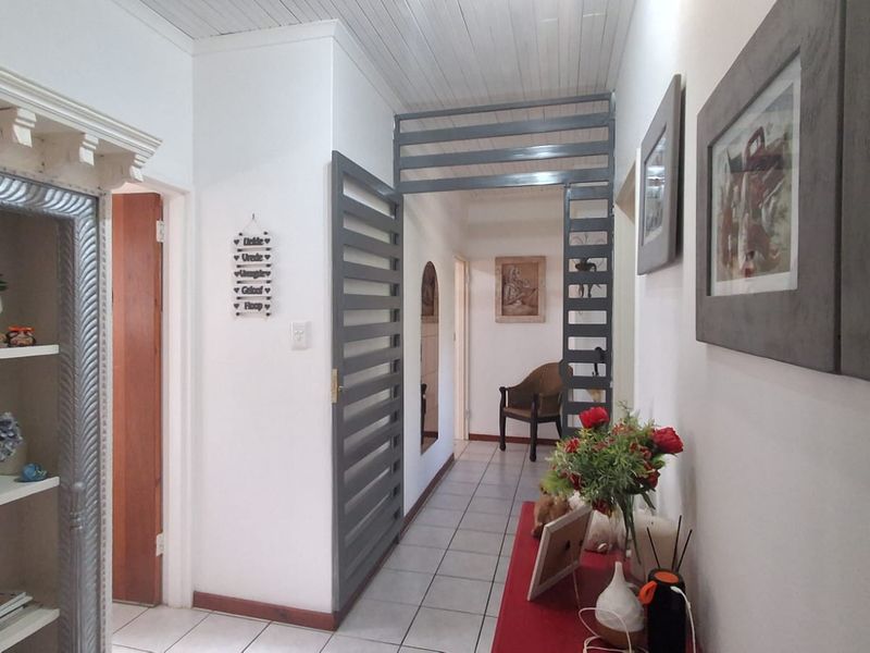 A bright hallway featuring tiled flooring, a timber tongue and groove ceiling, and a decorative slatted room divider.