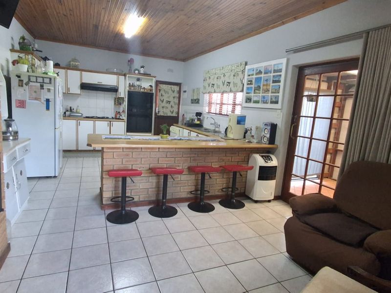 Open-plan kitchen and living area featuring a brick breakfast bar, tiled flooring, timber ceiling, and direct access to an outdoor patio area.