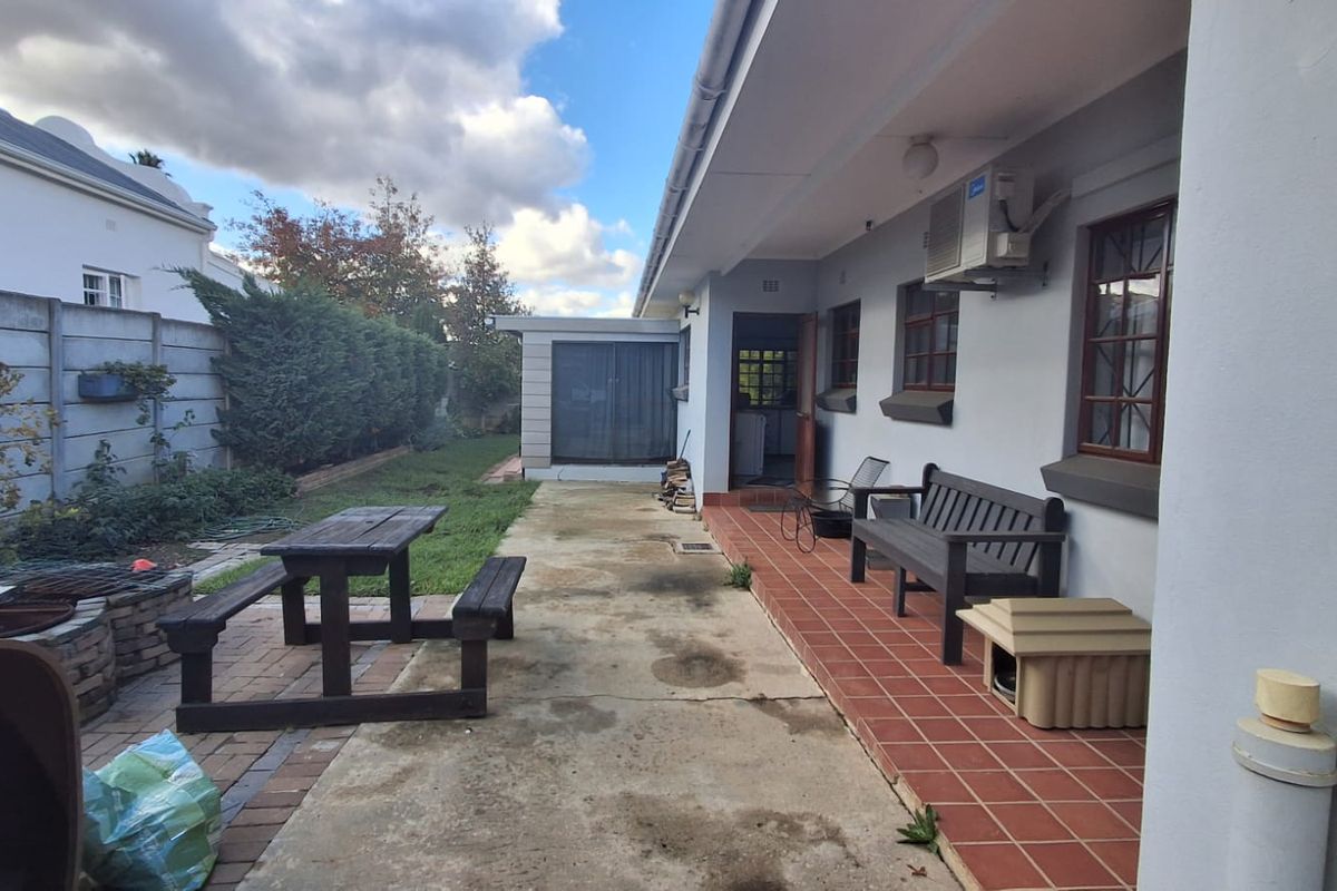 Rear exterior view featuring a tiled patio, concrete paving, and a brick fire pit area, providing a functional outdoor space for relaxation.