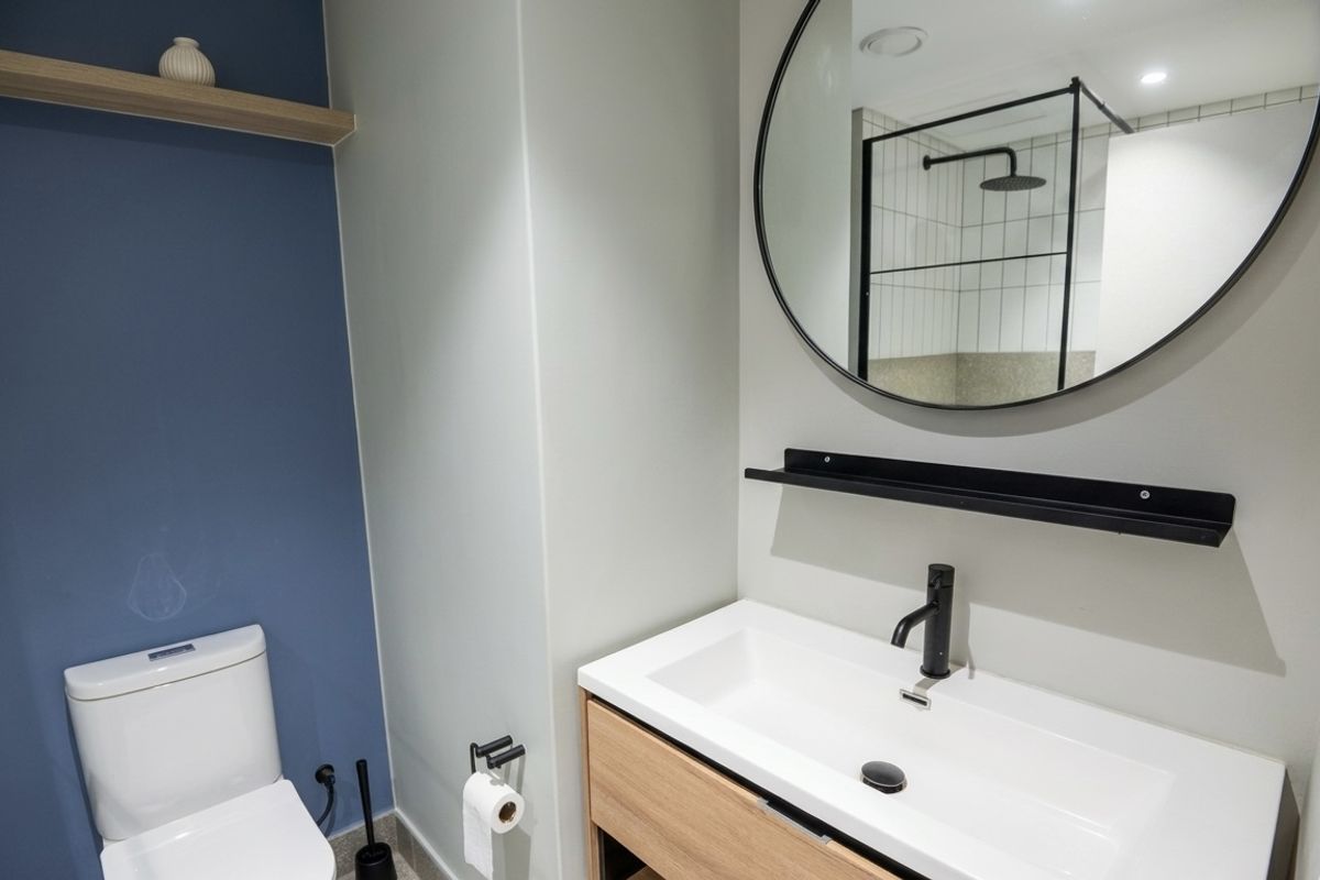 Modern bathroom featuring a timber vanity, black tapware, a round mirror, and a walk-in shower with a black frame and rain shower head.