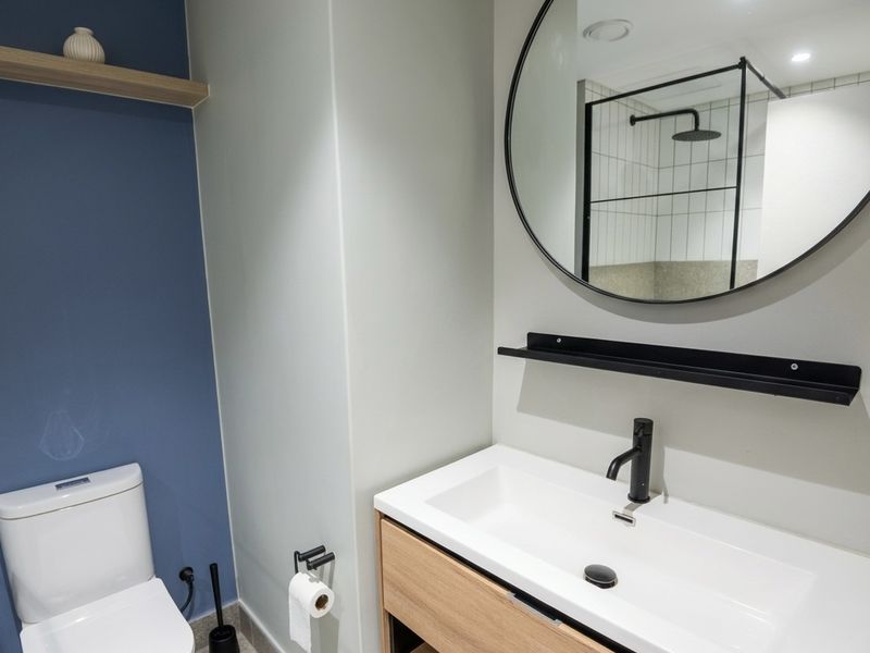 Modern bathroom featuring a timber vanity, black tapware, a round mirror, and a walk-in shower with a black frame and rain shower head.