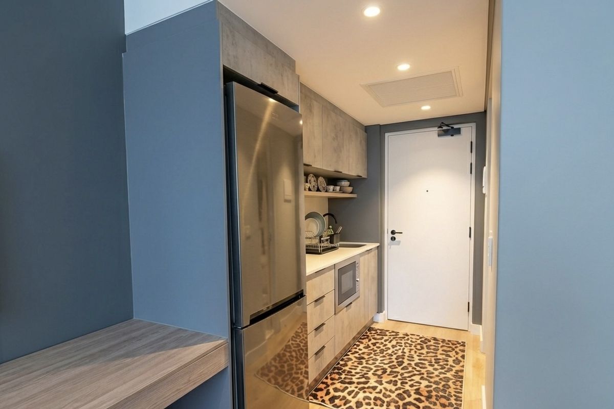 Compact modern kitchen featuring built-in cabinetry, integrated microwave, stainless steel refrigerator, and recessed lighting, conveniently located near the apartment entrance.